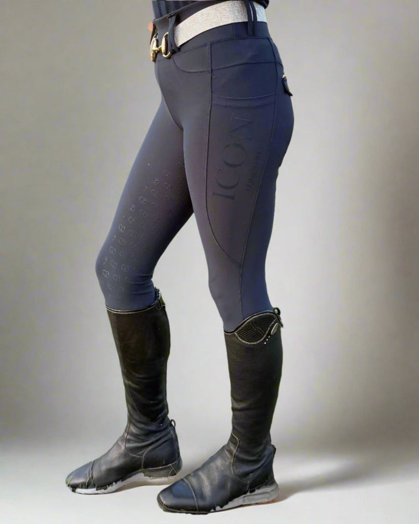 Person wearing gray riding pants with a visible brand logo, standing in a grassy field.